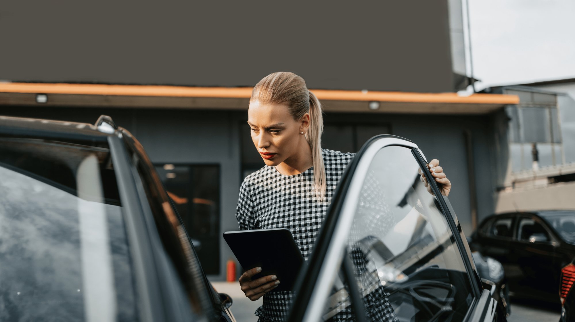 A female car dealership employee opens the door of a car and uses an AI-supported action list on a tablet to check the suggested improvements to the customer experience